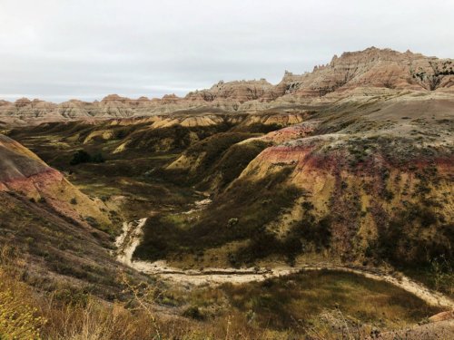 A scenic view of colorful, layered hills and a winding valley under a cloudy sky in a rugged landscape.