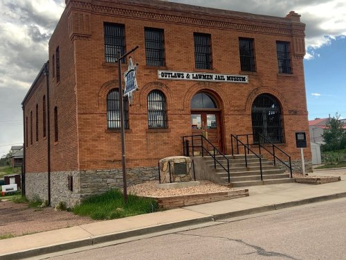 Brick building with a sign reading "Outlaws & Lawmen Jail Museum," featuring stairs and a stone foundation.