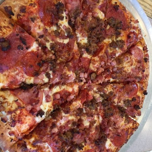 A large pizza topped with pepperoni, sausage, and diced ham, sliced into equal pieces on a silver tray.