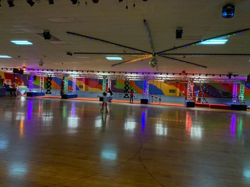 A spacious roller skating rink with colorful lights, a disco ball, and a vibrant mural on the walls.