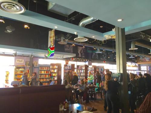 A busy café with bookshelves, people chatting, and a mural of Nelson Mandela on the wall.