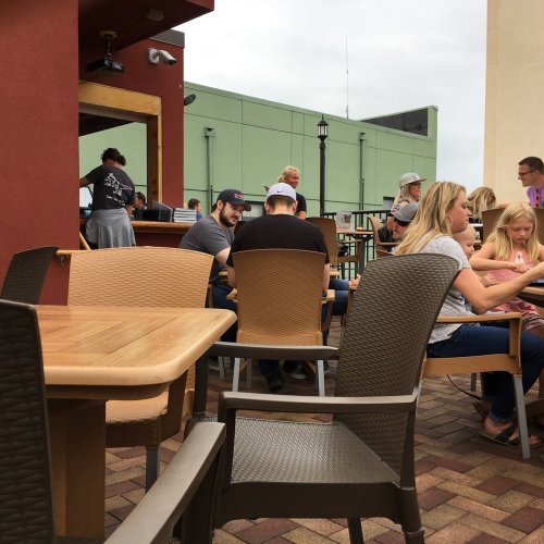 A casual outdoor dining area with people sitting at tables, enjoying food and drinks on a sunny day.