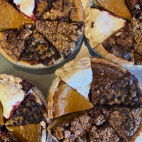 A variety of pie slices arranged on a table, including pumpkin, apple, and pecan pies.