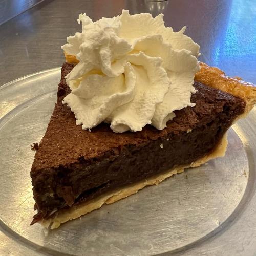 A slice of chocolate pie topped with a generous swirl of whipped cream on a silver plate.