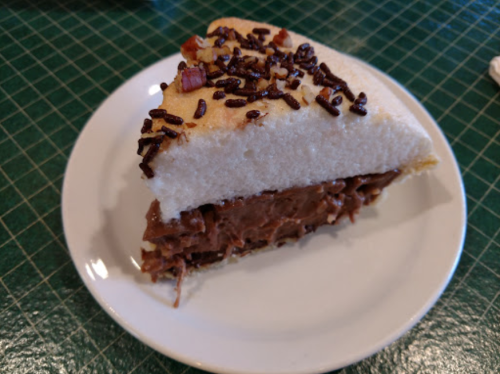 A slice of cake with chocolate filling, topped with chocolate sprinkles, on a white plate.