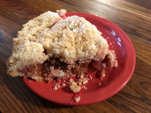 A slice of pie with a crumbly topping on a red plate, showcasing a fruit filling and a golden crust.