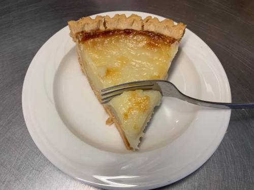 A slice of pie on a white plate, with a fork resting beside it, showcasing a golden, creamy filling and flaky crust.