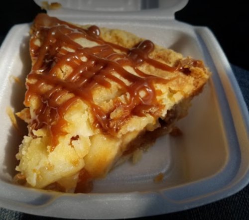 A slice of dessert with a golden crust, topped with caramel drizzle, served in a takeout container.