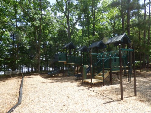 A playground with slides and climbing structures surrounded by trees and a sandy area.