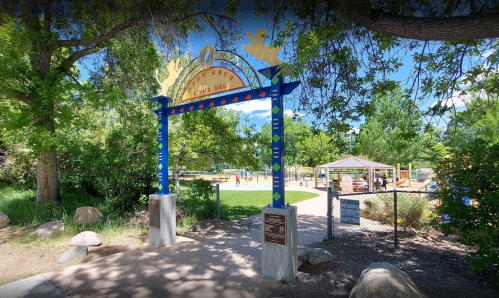 Colorful entrance archway to a park, surrounded by trees, leading to a playground in the background.