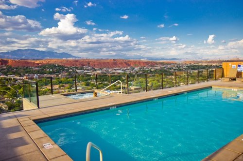 A rooftop pool with a stunning view of mountains and a cityscape under a blue sky with fluffy clouds.