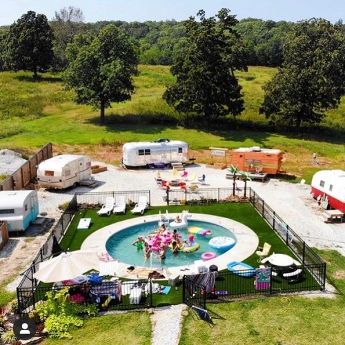 Aerial view of a pool area surrounded by trailers, with people enjoying the water and lounging on colorful floats.