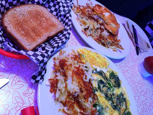A breakfast spread featuring an omelette, hash browns, a croissant, and toasted bread on a patterned table.