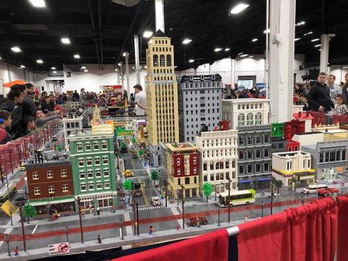 A detailed LEGO cityscape with buildings, streets, and mini figures, displayed at a crowded event.