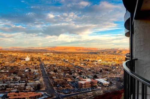 A panoramic view of a town with mountains in the background, under a colorful sky at sunset.