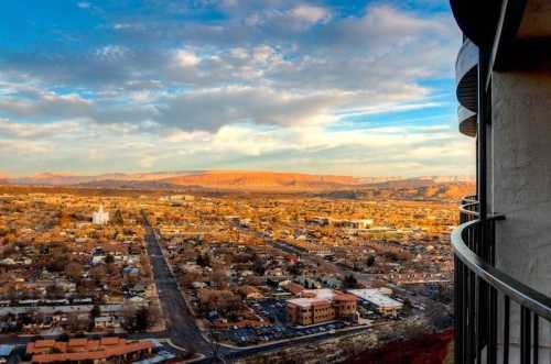 A panoramic view of a town with mountains in the background, under a colorful sky at sunset.