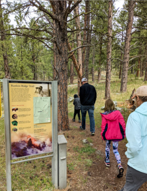 A family walks along the Rankin Ridge Trail, passing an informational sign in a forested area.