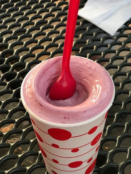 A cup of pink yogurt or smoothie with a red spoon, placed on a black metal table.