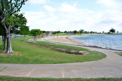 A scenic view of a beach area by a lake, with grassy paths, trees, and people enjoying the outdoors.