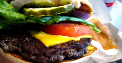 Close-up of a juicy hamburger with lettuce, tomato, pickles, onions, and melted cheese on a toasted bun.
