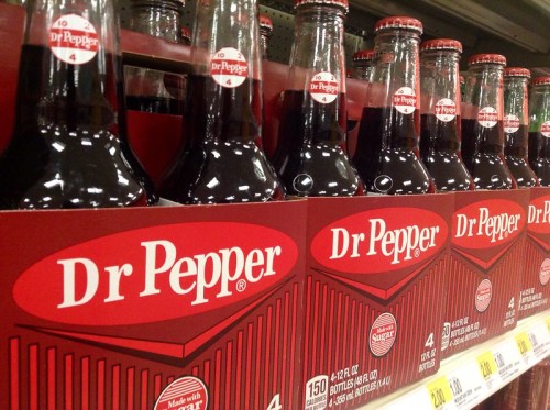 A row of Dr Pepper soda bottles on a store shelf, featuring the iconic red label and logo.