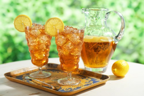 Two glasses of iced tea with lemon slices, served on a decorative tray alongside a pitcher and a lemon.