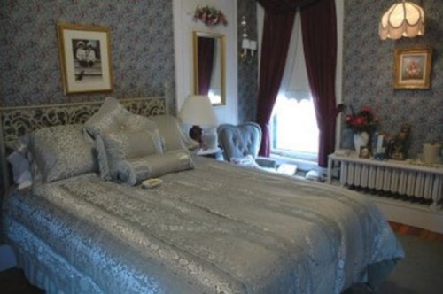 A cozy bedroom featuring a large bed with silver bedding, elegant curtains, and vintage decor.
