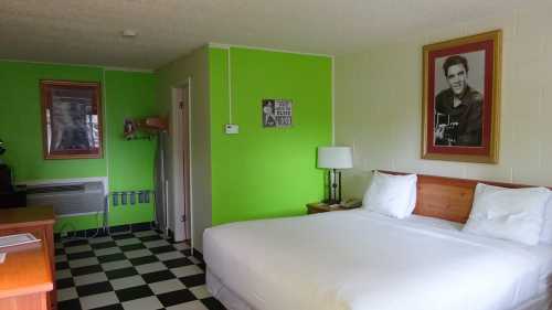 A brightly colored hotel room with a double bed, checkered floor, and a large framed portrait on the wall.