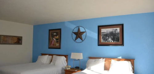 A hotel room with two beds, blue walls, and framed artwork featuring a star and historical images.