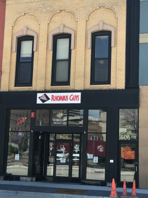 Exterior of a building featuring the "Rhombus Guys" sign, with large windows and a brick facade.