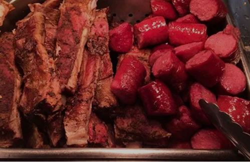 A serving tray with grilled ribs and sliced sausages, both seasoned and cooked to a rich brown color.