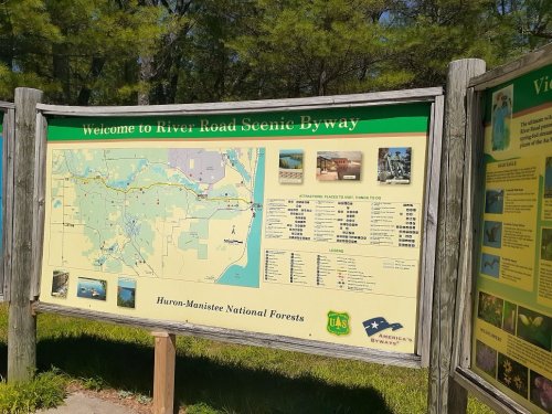 Signboard welcoming visitors to River Road Scenic Byway, featuring a map and information about attractions in Huron-Manistee National Forests.
