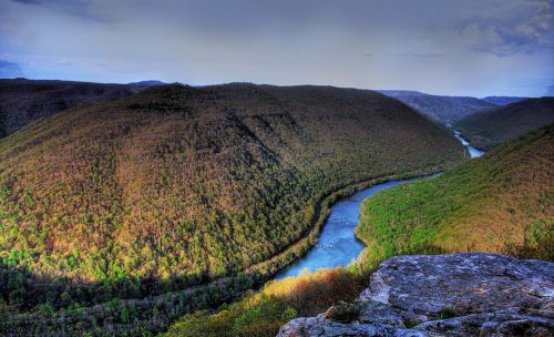 A scenic view of a winding river surrounded by lush green hills under a partly cloudy sky.