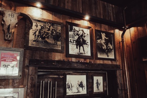 A rustic wooden wall displays vintage black-and-white rodeo photographs and a cow skull.