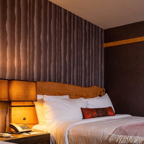 A cozy hotel room featuring a bed, decorative pillows, a bedside lamp, and textured wall design.