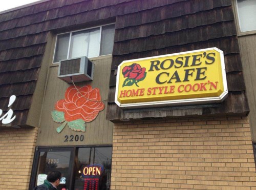 Exterior of Rosie's Cafe, featuring a large sign with a rose and the text "Home Style Cook'n." Open for business.