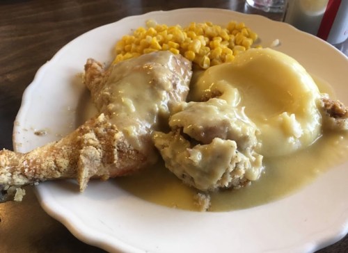 A plate of fried chicken with gravy, mashed potatoes, and corn on the side.