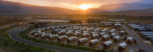 Aerial view of a modern housing development at sunset, with rows of homes and mountains in the background.