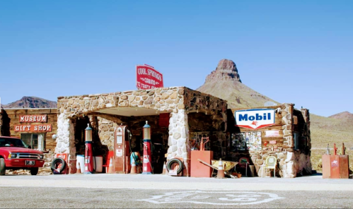 A vintage stone gas station with a gift shop, surrounded by desert landscape and a mountain in the background.