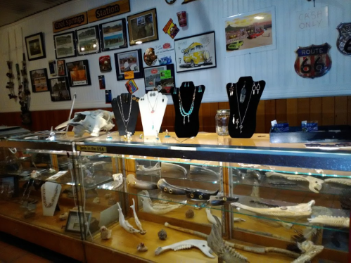 Display case with jewelry and souvenirs, surrounded by Route 66 memorabilia and decorative items on the walls.