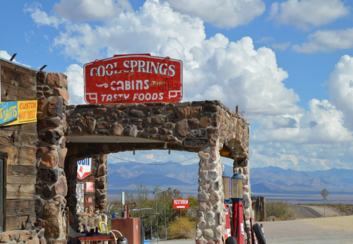 Sign for Cool Springs Cabins and Tasty Foods, with a rustic stone archway and mountains in the background under a cloudy sky.