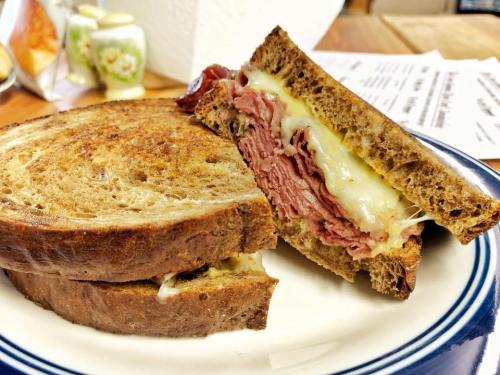 A close-up of a toasted sandwich with layers of meat and melted cheese, served on a white plate.