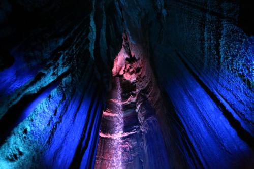 A colorful cave interior with blue and purple lighting illuminating the textured rock formations above.