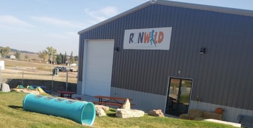 A gray building with a colorful "RNHILD" sign, featuring a playground area with a tunnel and picnic tables outside.