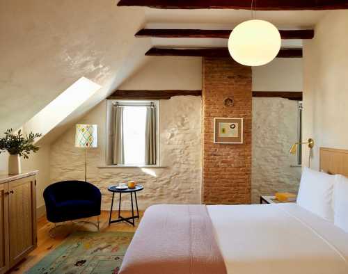 Cozy attic bedroom with a bed, a small table, a chair, and a brick accent wall, featuring natural light from a skylight.