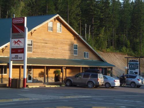A wooden building with a green roof, gas station sign, and parked cars in a forested area.