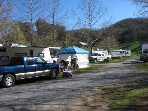 A campsite with several RVs and a blue tent, surrounded by trees and hills under a clear blue sky.