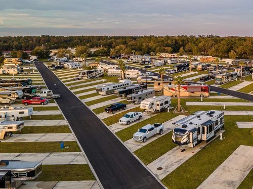 Aerial view of a large RV park with numerous parked trailers and vehicles, surrounded by trees and open spaces.