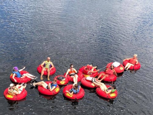 A group of people relaxing on red inner tubes in a calm body of water on a sunny day.