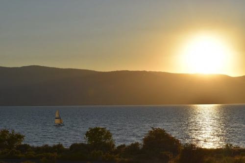 A sailboat glides across a shimmering lake at sunset, with mountains silhouetted in the background.